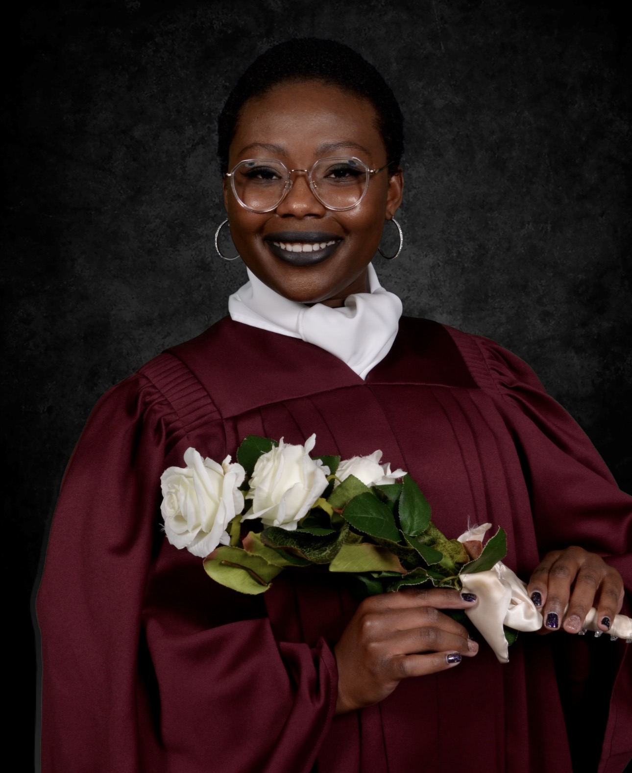 Inès Zongo diplômée, en toge bordeaux, tenant un bouquet de roses blanches
